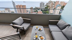 Un balcón con sofá, una mesita y vistas a la ciudad y al océano.
