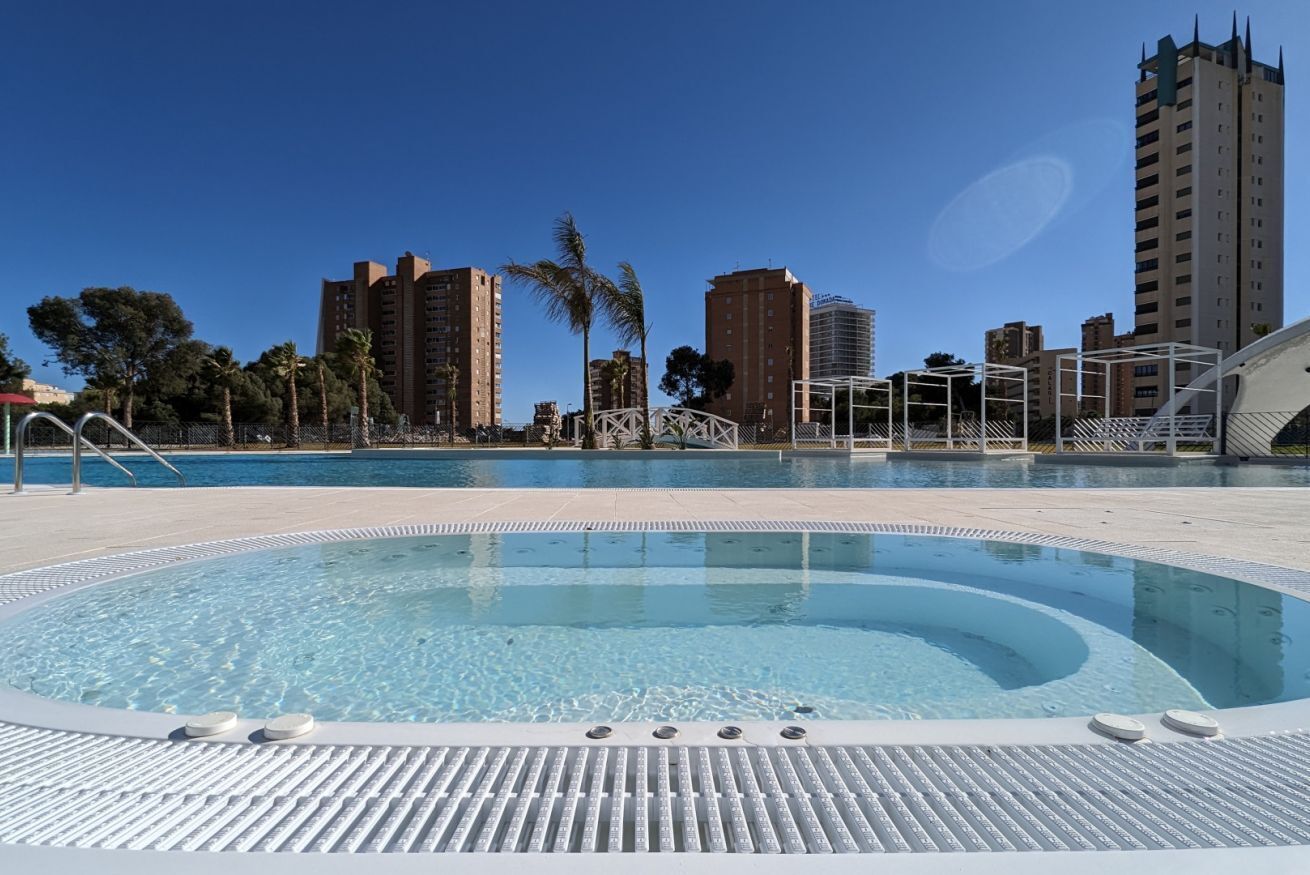 A swimming pool with a hot tub, palm trees, and tall buildings in the background.