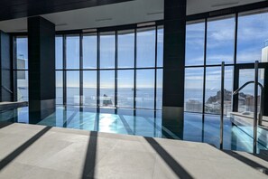 Une piscine intérieure moderne dotée de grandes baies vitrées offrant une vue sur la ville.