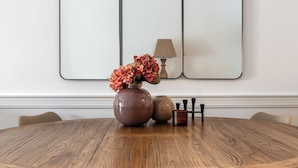 Une table de salle à manger ronde en bois, ornée d’un vase de fleurs, d’une lampe et d’un ensemble de couverts.