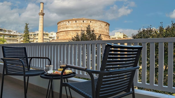 Un balcon avec deux chaises et une table, d’où l’on peut admirer une tour historique et un bâtiment circulaire.