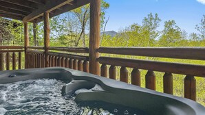 Un bain à remous sous une pergola en bois, avec vue sur des arbres verdoyants et une montagne en arrière-plan.