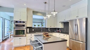 Una cocina moderna con electrodomésticos de acero inoxidable, una isla central con taburetes altos e iluminación colgante.