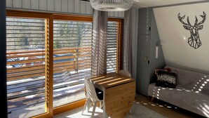 Habitació moderna amb grans finestres, un escriptori de fusta, un sofà i una decoració de cap de cérvol penjada a la paret.