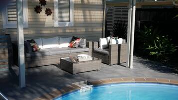 A covered outdoor seating area with a pool, featuring a sofa and chairs, and a pergola overhead.
