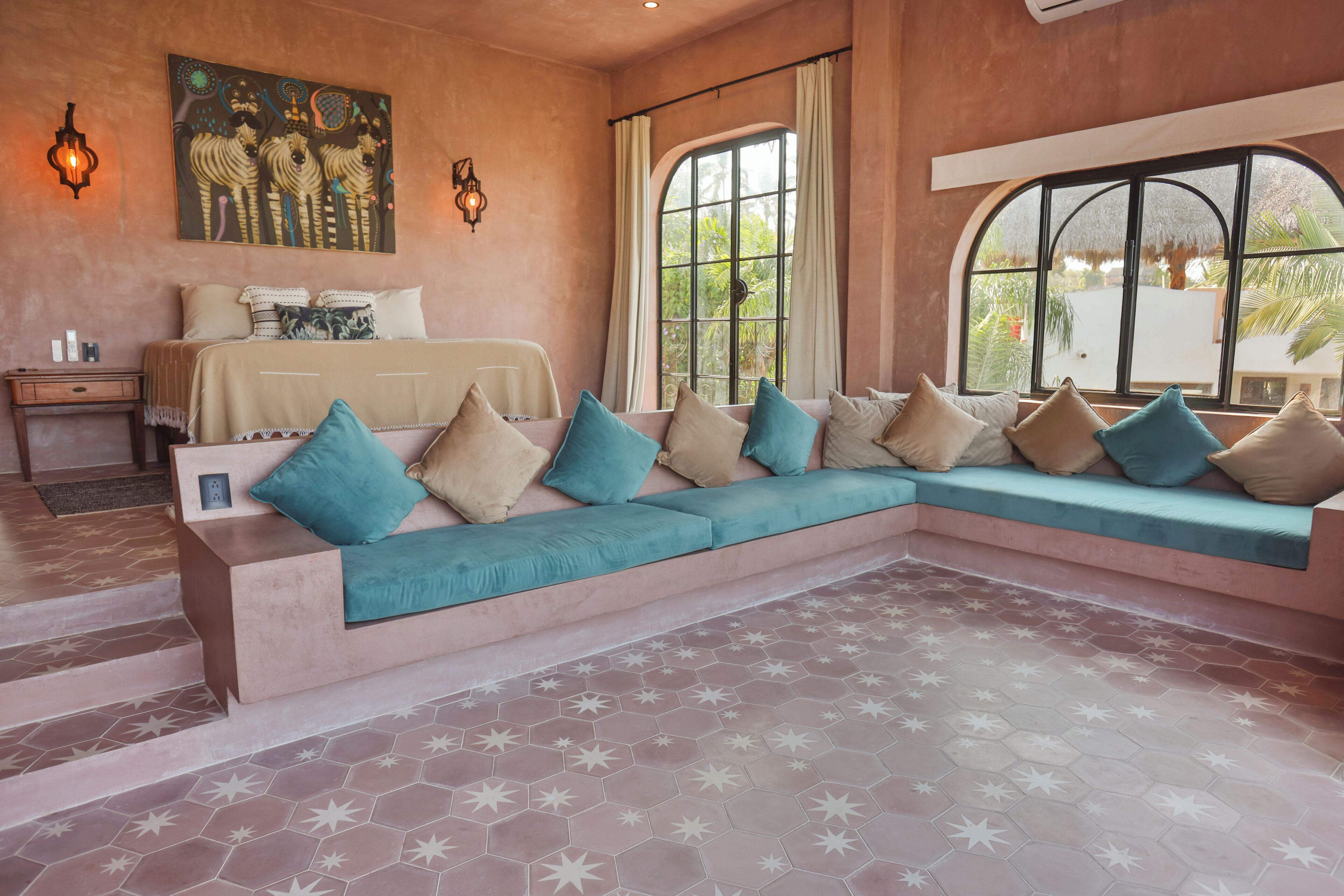 A room with a large sofa, a bed, a nightstand, and a window with curtains.
