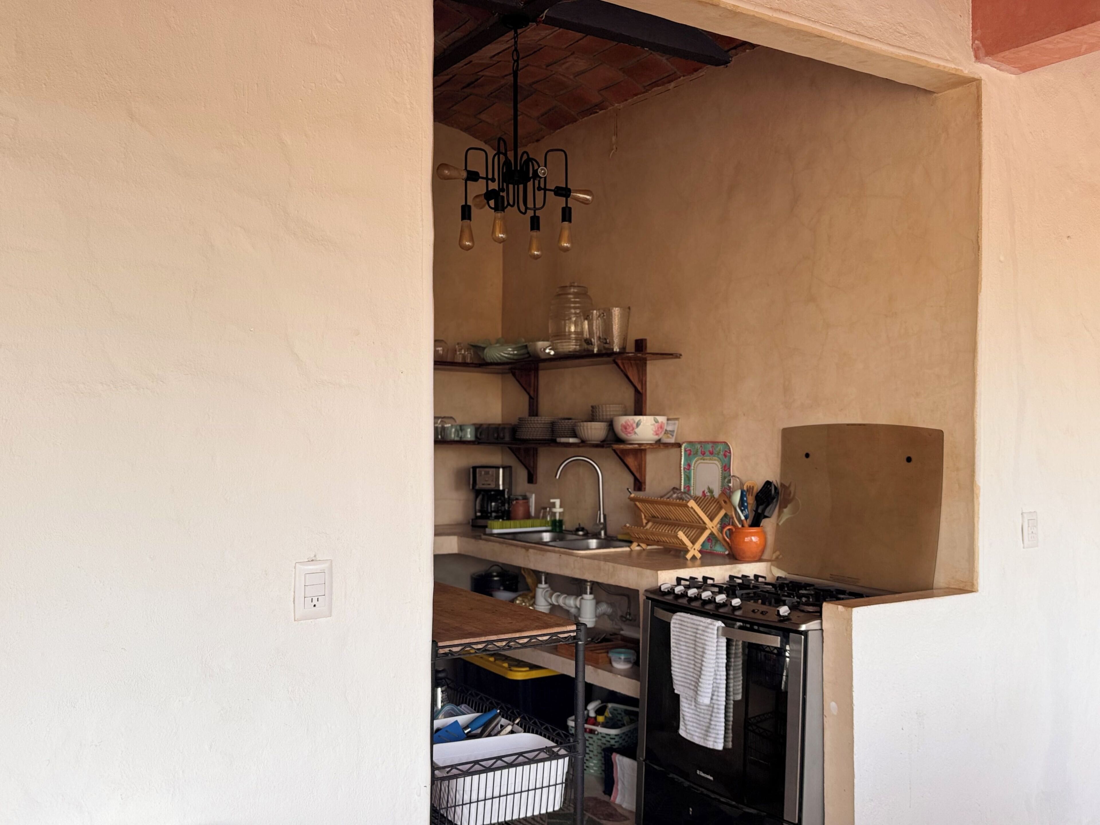 A compact kitchen with a stove, sink, and hanging light fixture.