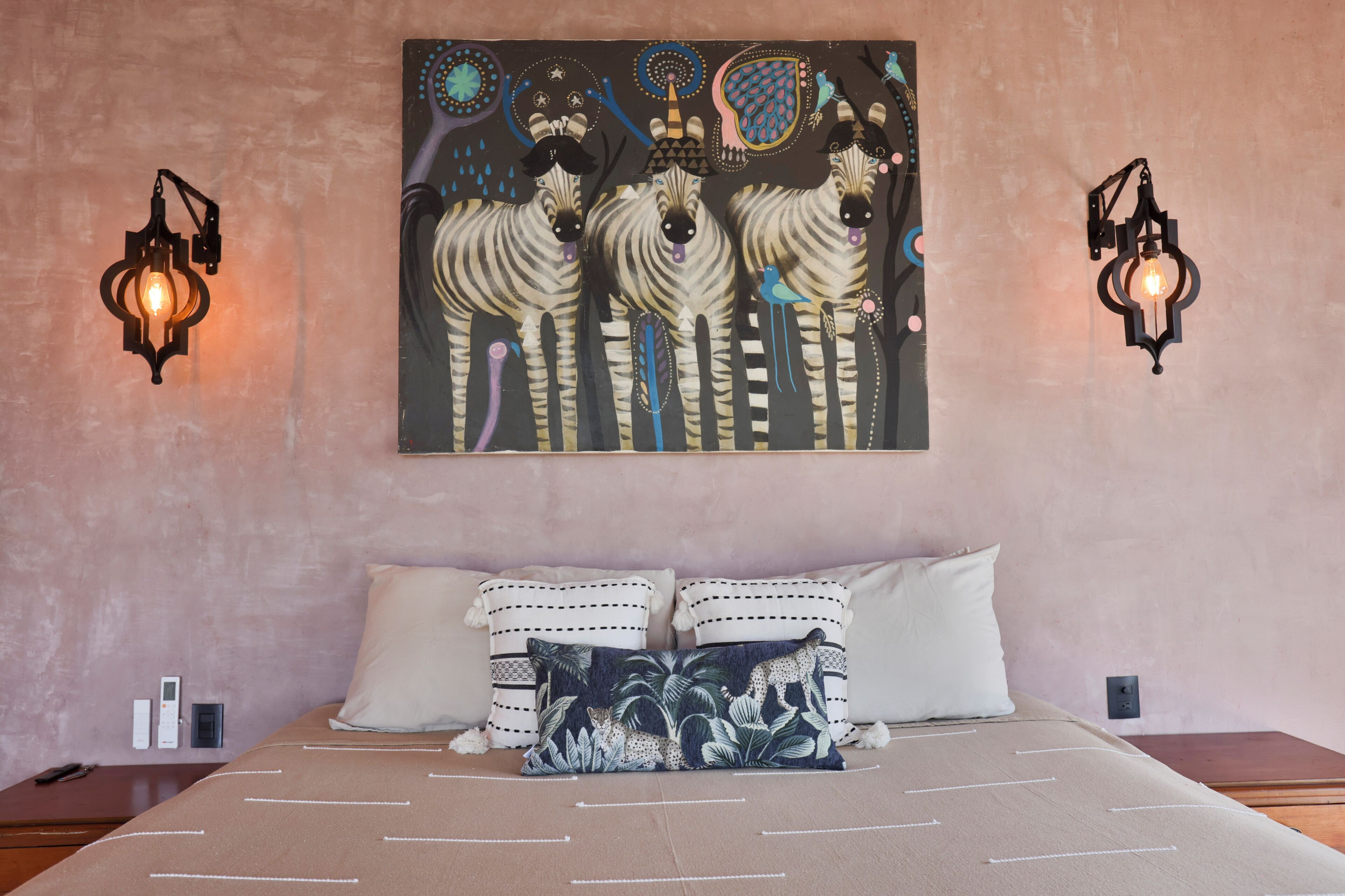 Quarto com cama, almofadas, pintura de zebra na parede e duas arandelas.