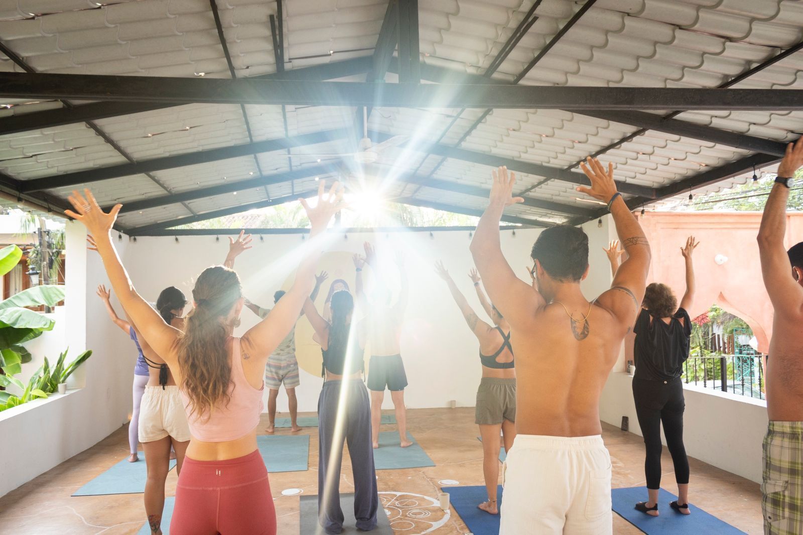 Un grupo de personas en un espacio al aire libre techado, posiblemente una clase de yoga o entrenamiento físico, con techo y paredes de metal.