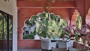 Zona de menjador amb caires de vimet i taula per a dues persones, envoltada de plantes tropicals exuberants i una arc decoratiu.