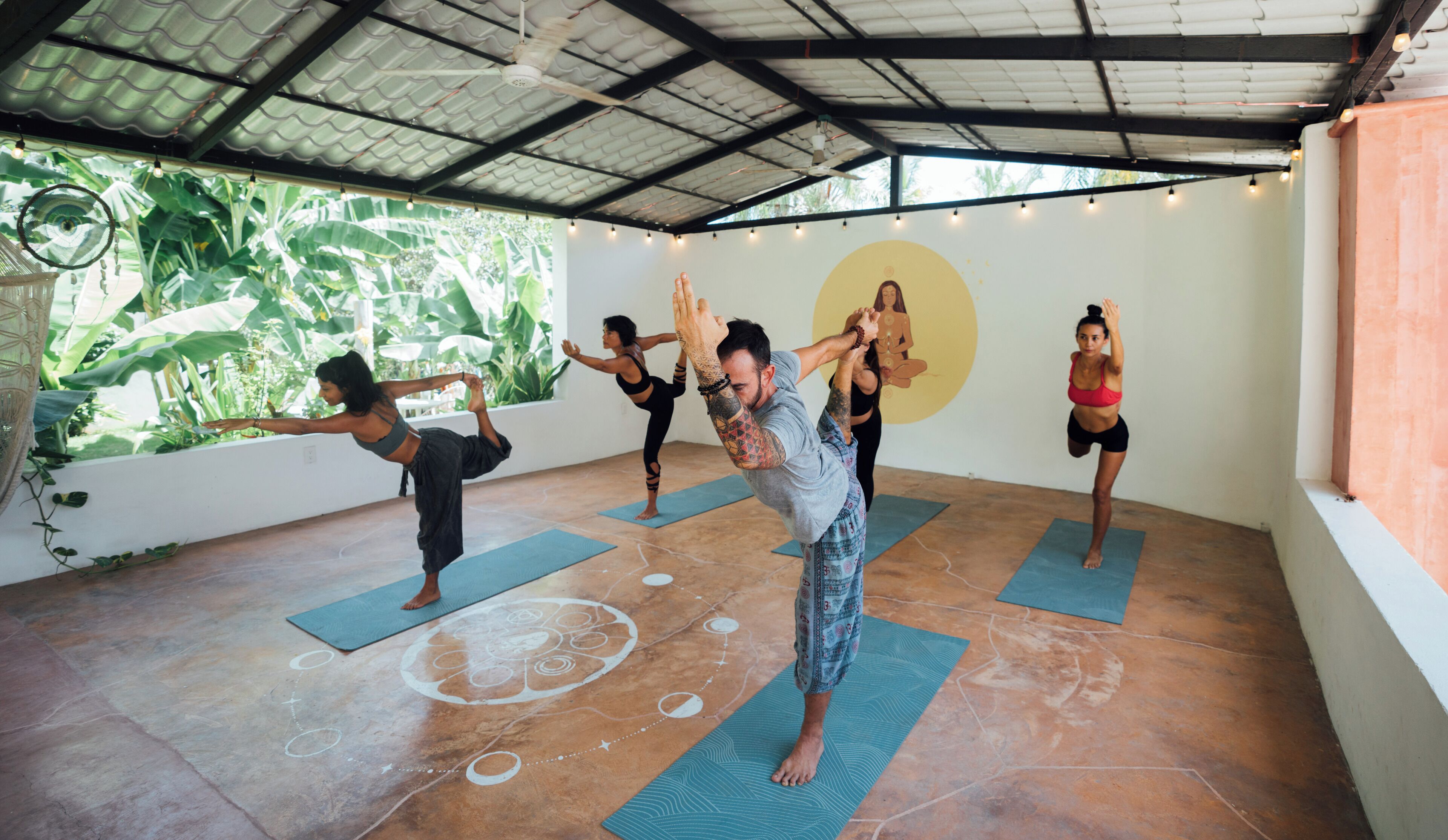 A yoga class in a room with a high ceiling and large windows, allowing natural light to enter.