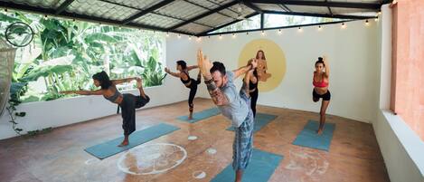 A yoga class in a room with a high ceiling and large windows, allowing natural light to enter.