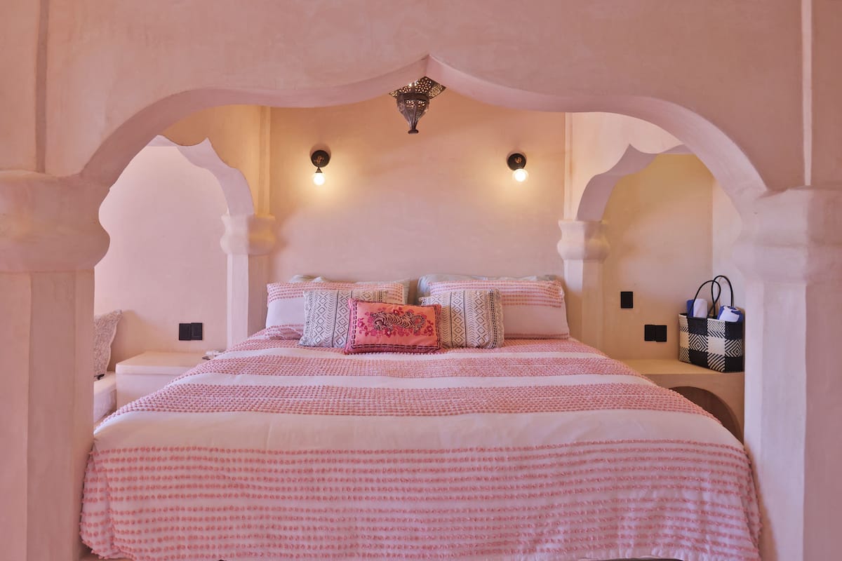 Un dormitorio con una cama grande, dos luces fijadas a la pared y un detalle decorativo en el techo.