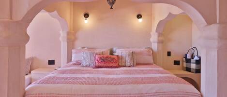 Een slaapkamer met een groot bed, twee wandlampen en een decoratief plafond.