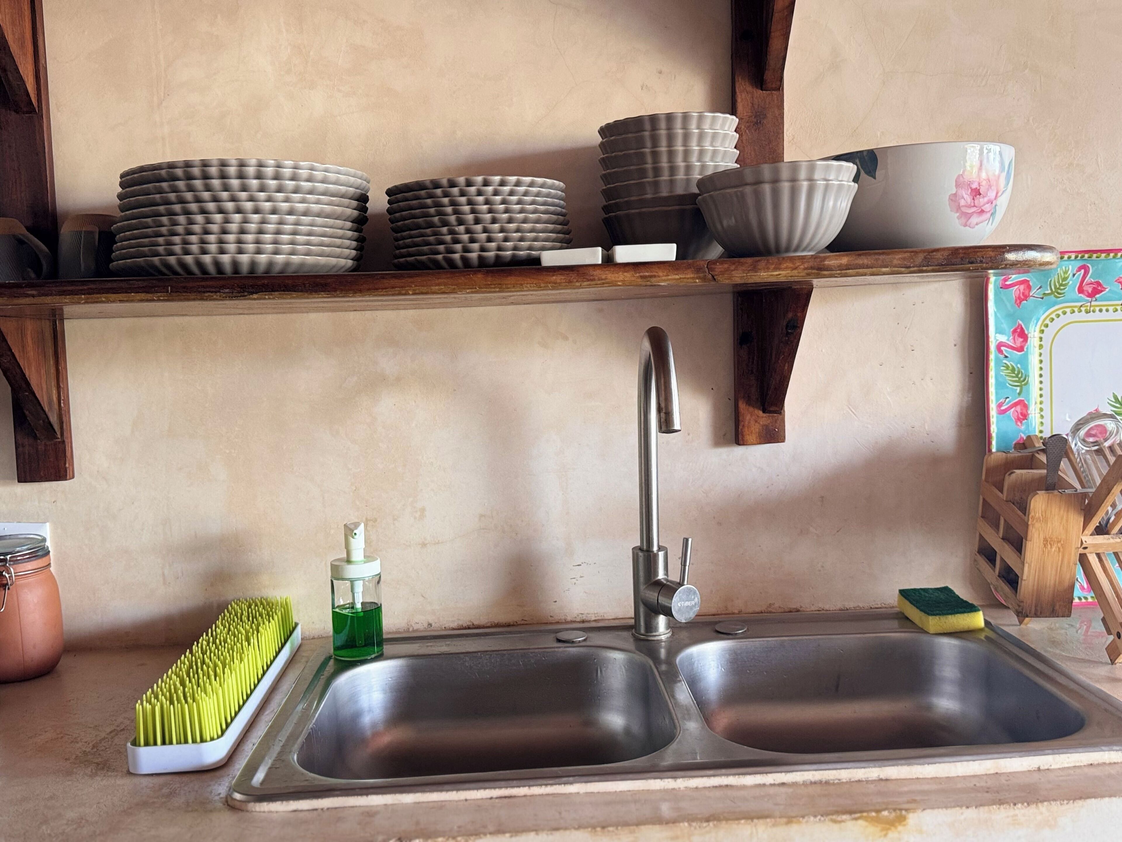 A kitchen with a double sink, a dish rack with plates, a jar of dish soap, and a sponge.