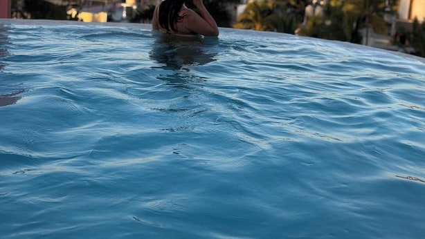 Una persona relaxant-se en una piscina amb vista a l'oceà i a les colines de fons.