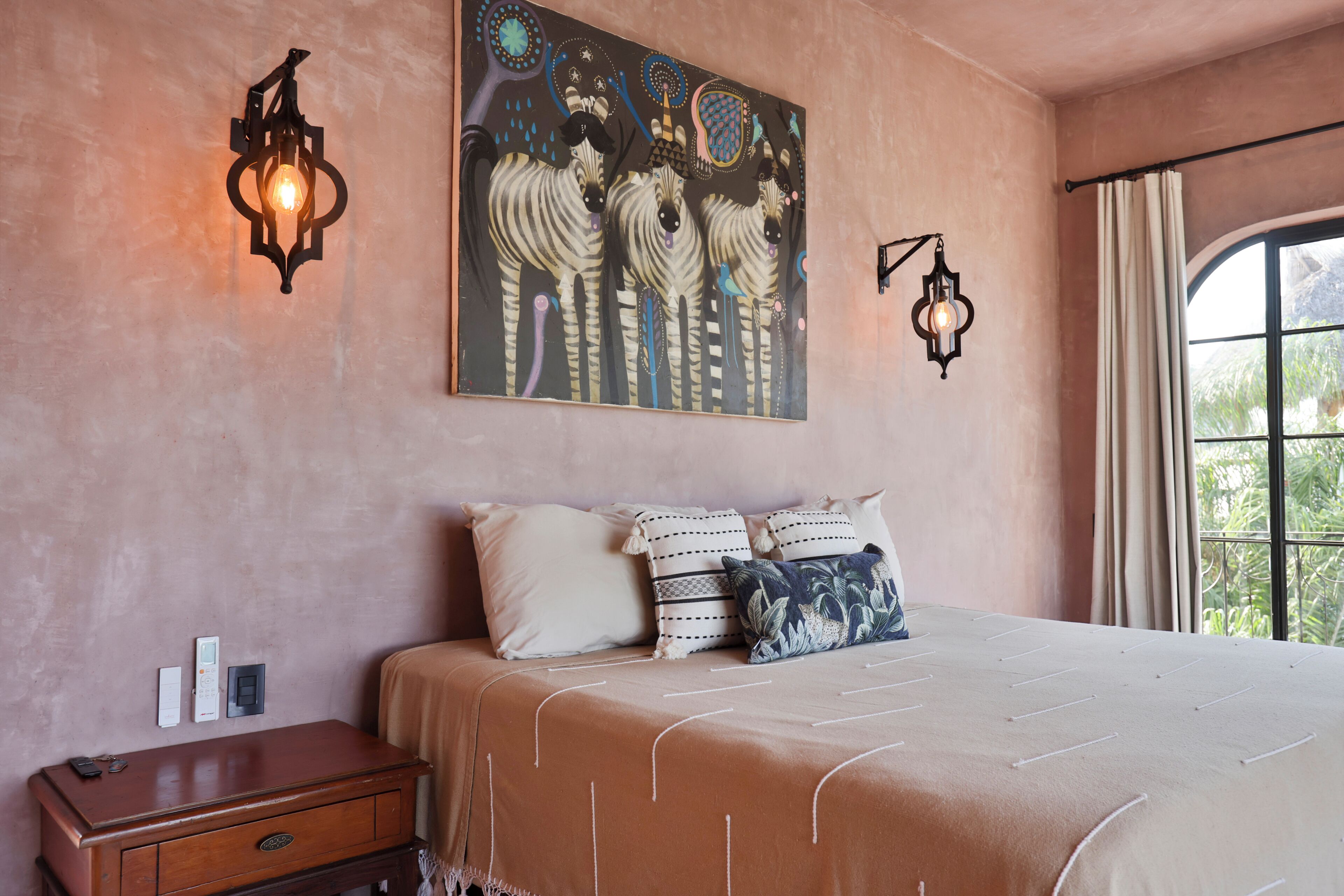 A bedroom with a bed, pillows, a nightstand, wall sconces, and a painting.