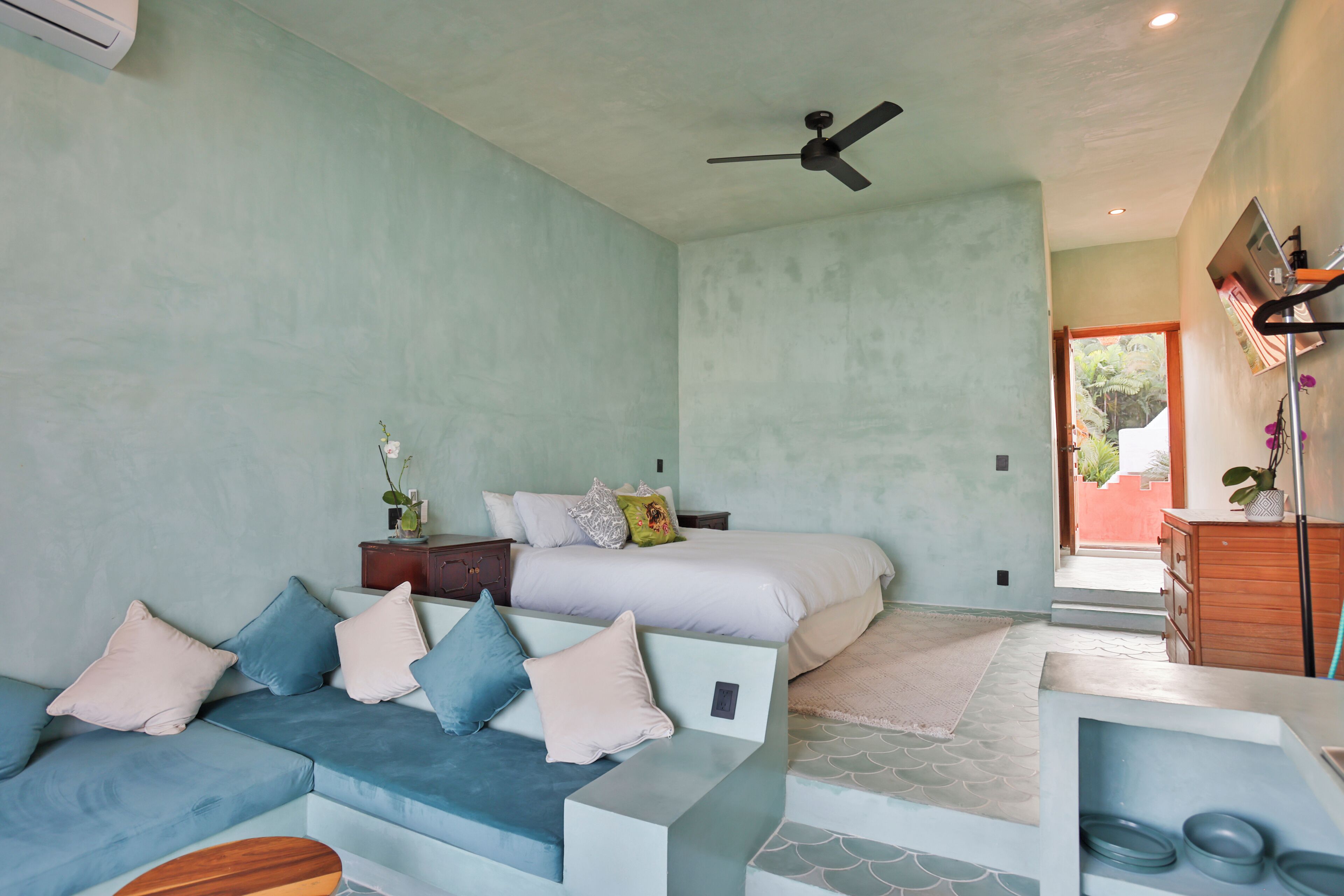 Une chambre à coucher moderne avec un lit, un canapé, un ventilateur de plafond et une vue sur l’extérieur.
