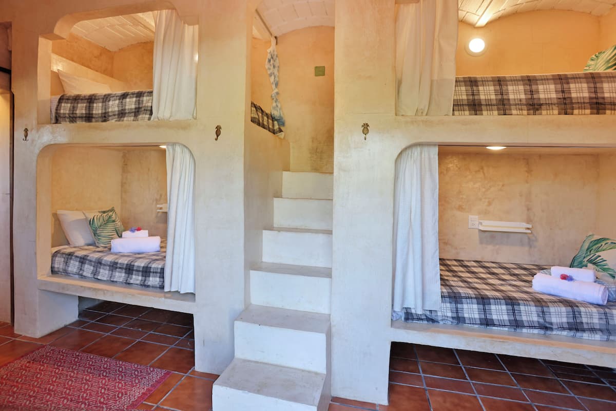 Habitación tipo dormitorio con literas, una escalera y una alfombra roja estampada.
