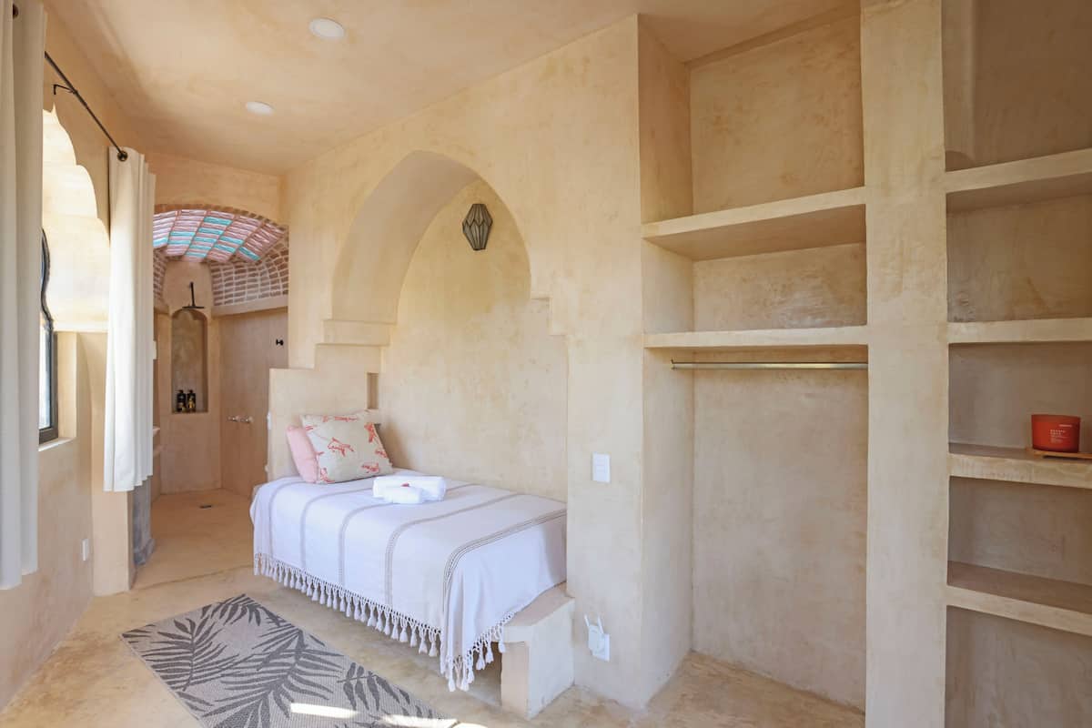 Un dormitorio con cama, un estante pequeño y un rincón ducha.