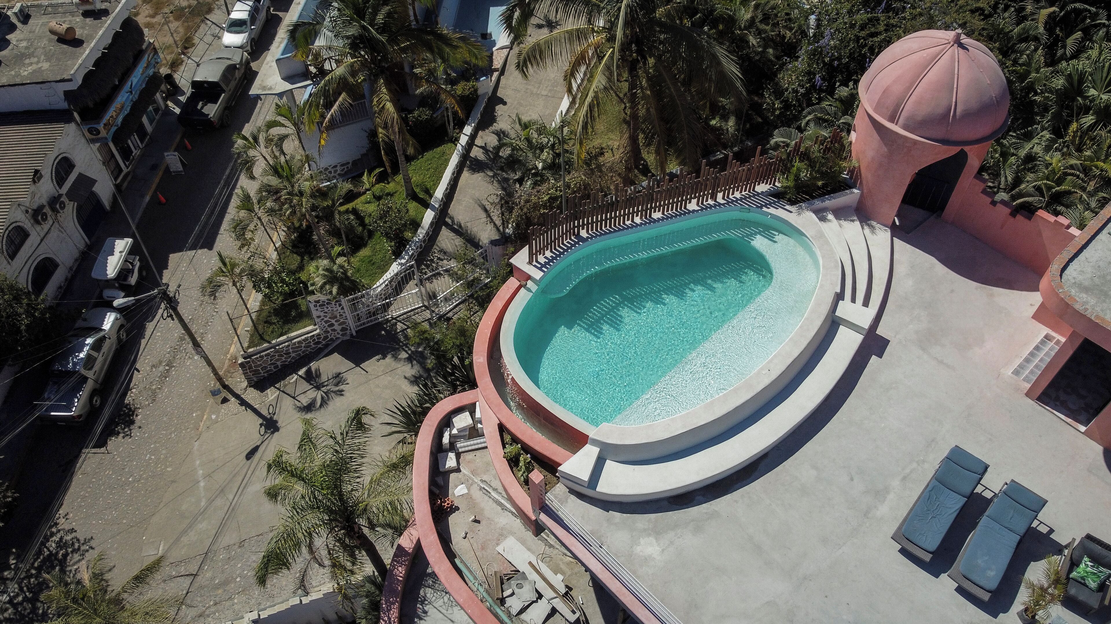 An aerial view of a resort with a circular pool, palm trees, and a gazebo.