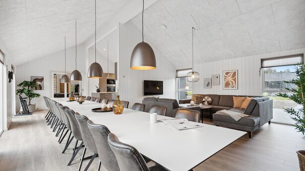 Un salón espacioso con una larga mesa de comedor, diversas opciones de asiento e iluminación colgante moderna.