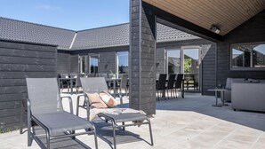 Un espacio de patio al aire libre con sillas y un sofá de metal, una zona de estar cubierta y vista de la casa al fondo.