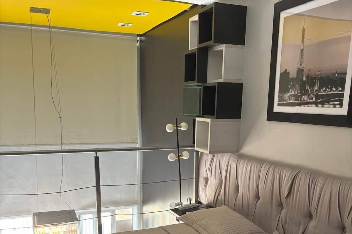 Ein modernes Schlafzimmer mit einem großen Bett, Blick auf die Stadt und einer gelben Akzentwand.