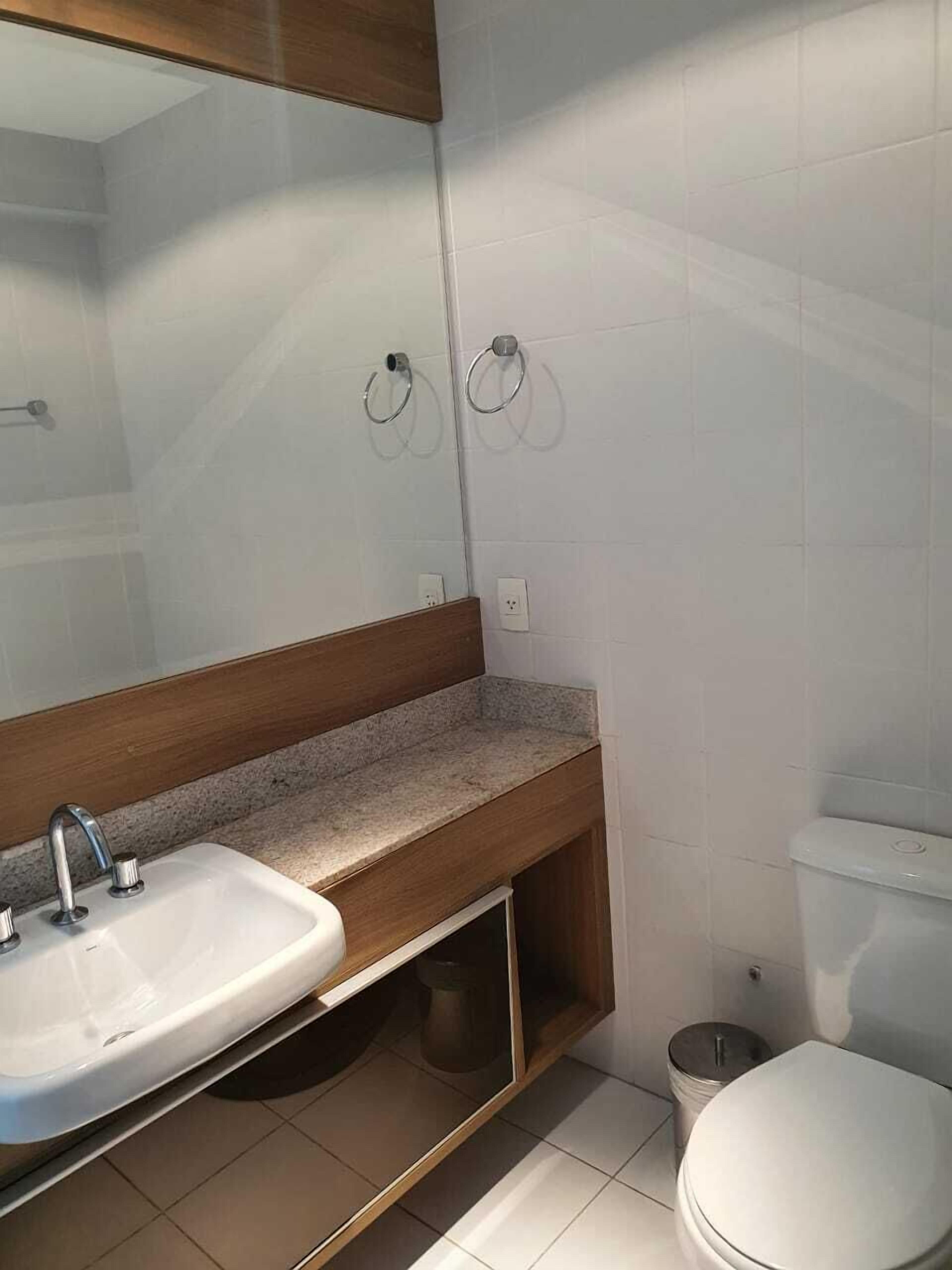 A bathroom with a sink, mirror, toilet, and a trash bin.