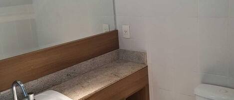 A bathroom with a sink, mirror, toilet, and a trash bin.