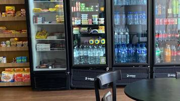 A row of beverage dispensers labeled 'FROZEN' and 'FRESH' in a food service area with wooden flooring and black chairs.