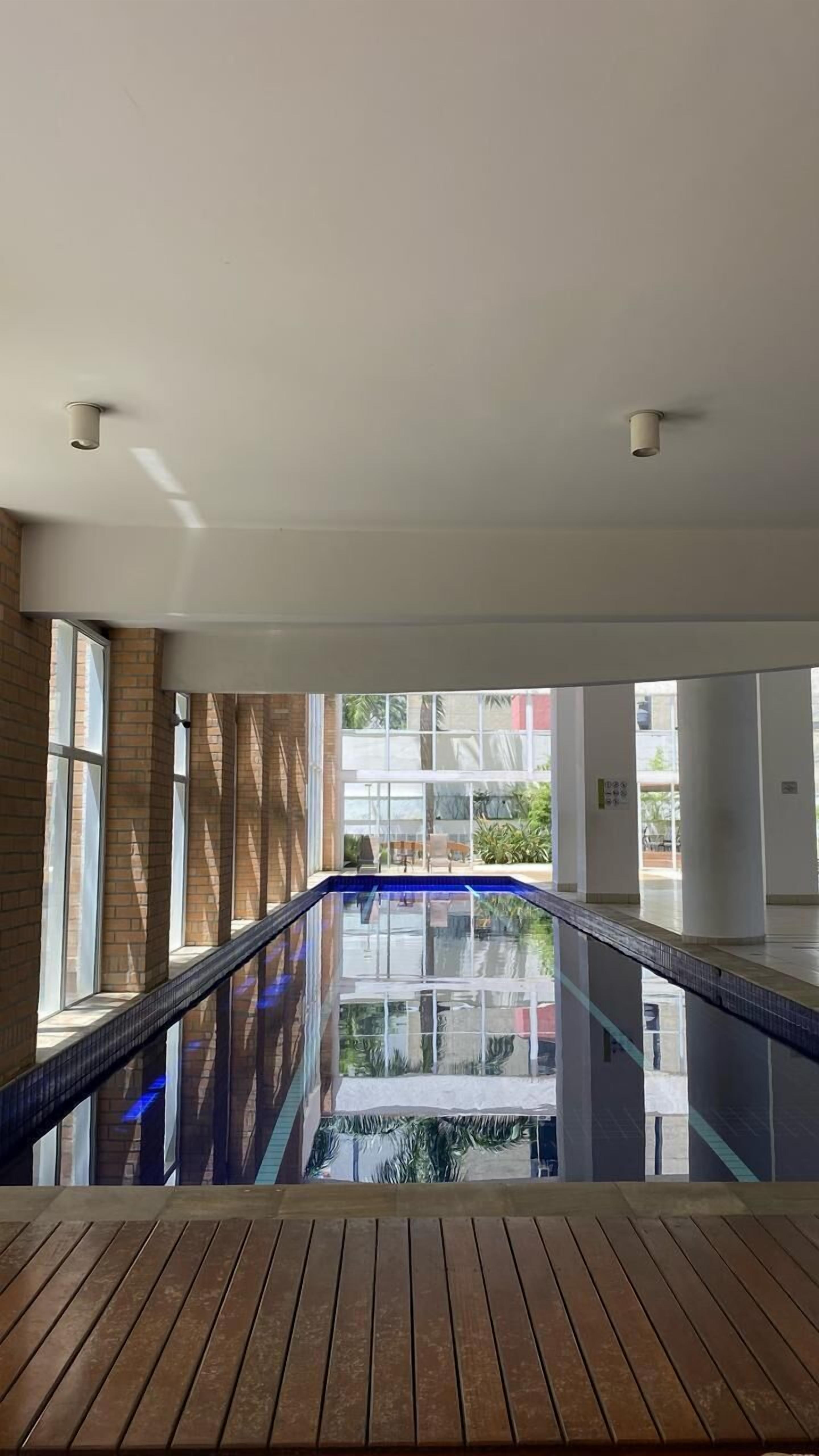 A modern indoor pool area with a wooden deck and glass walls.