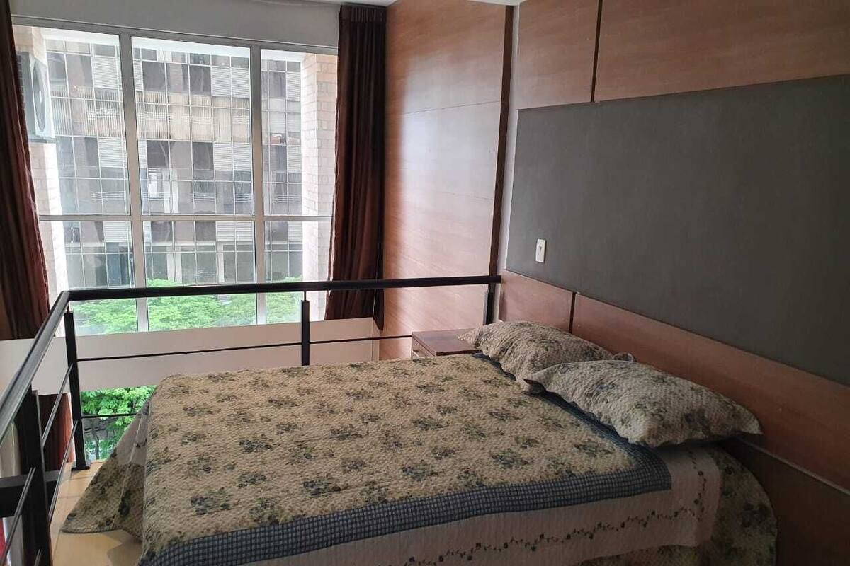 Ein Schlafzimmer mit einem großen Bett, einem Fenster mit Vorhängen und Blick auf Gebäude.