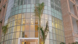 A modern hotel with a curved glass facade, a visible entrance, and a black car parked in front. - NYC Residence Flat condominio (São Paulo)