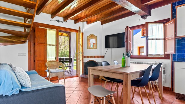 Un interior acogedor con una mesa de comedor de madera, sillas, un sofá y un televisor montado en la pared.