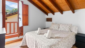 Un dormitorio con techo de madera, una cama con colcha estampada, una mesita de noche y una ventana con vistas a las montañas.