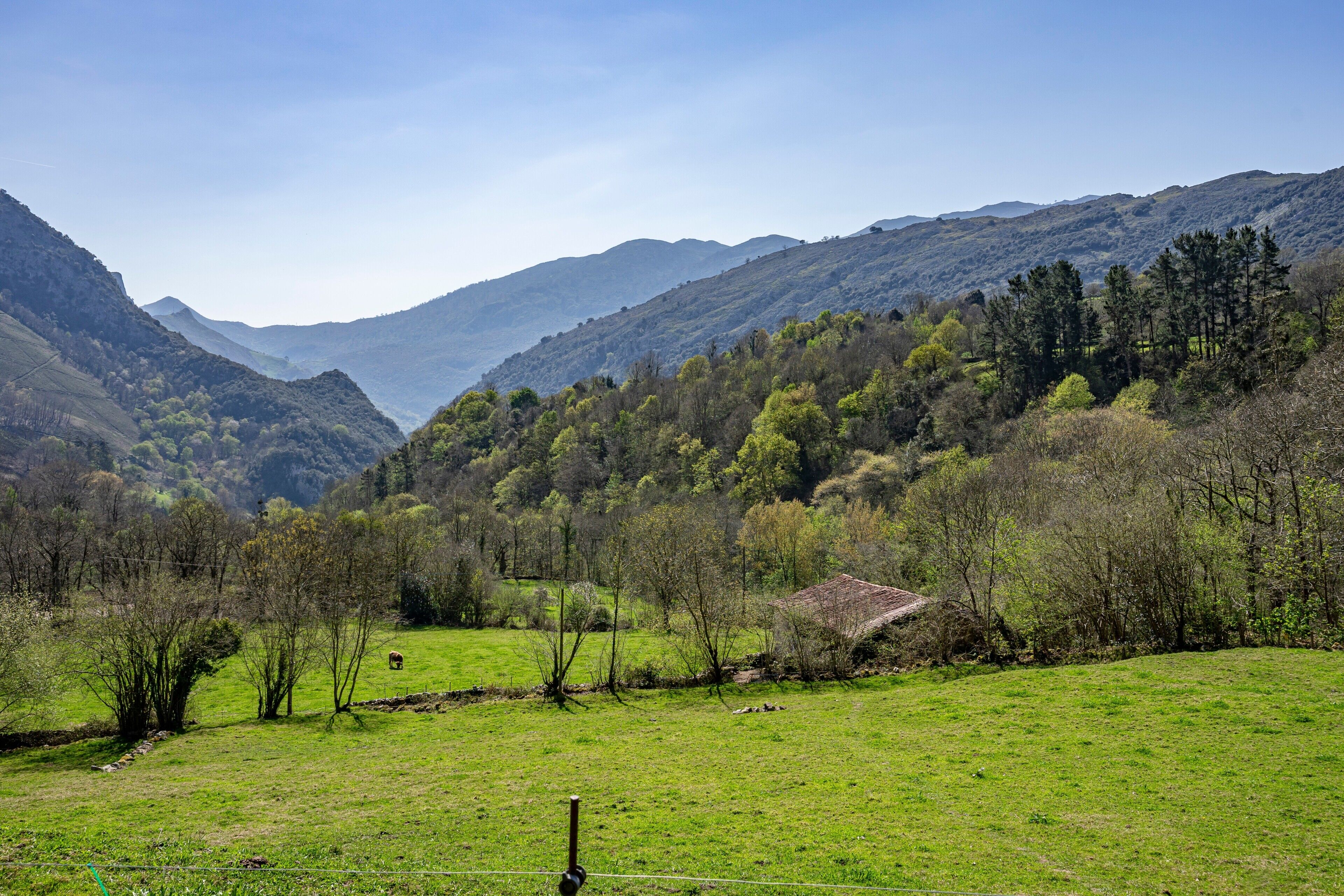 Paisagem montanhosa com um campo gramado, um muro de pedra e um pequeno edifício.