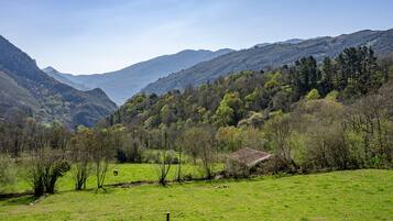 Paisagem montanhosa com um campo gramado, um muro de pedra e um pequeno edifício.