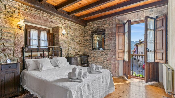 A stone-walled bedroom with a wooden ceiling, a bed with white linens, a nightstand, a mirror, and a view through an open door. - Apartment 'La Breval' with Mountain View, Private Terrace and Private Garden (Alles)