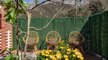 Un espace patio avec trois chaises en osier, un mur en briques et une haie.