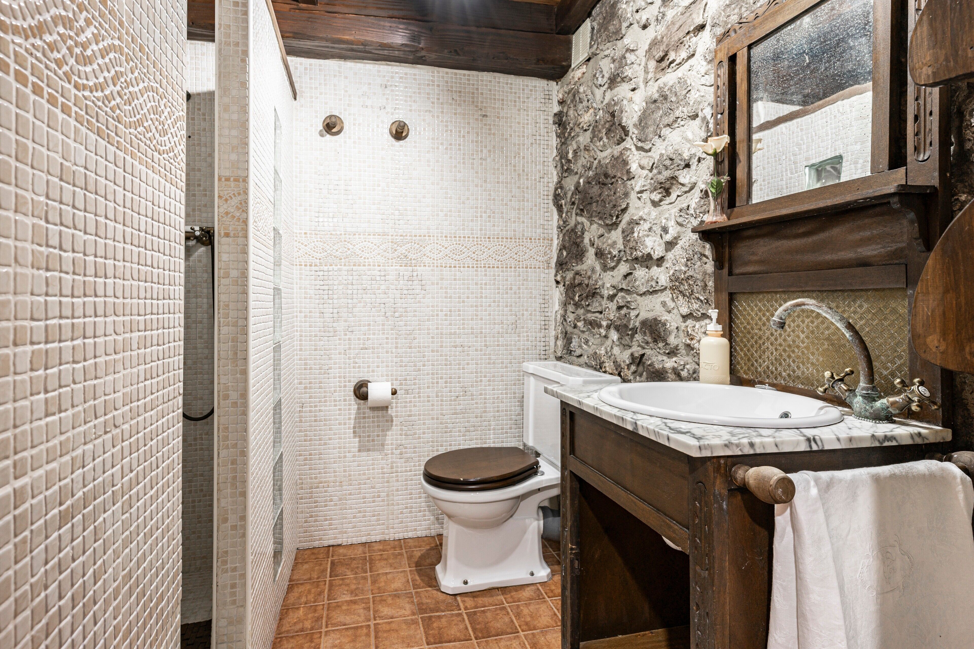 Un baño con inodoro blanco, lavabo con encimera de mármol y zona de ducha con pared azulejada.