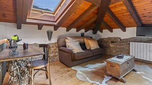 A cozy loft-style room with a wooden ceiling, a stone wall, a sofa, a small table, and a cowhide rug. - Apartment 'La Breval' with Mountain View, Private Terrace and Private Garden (Alles)