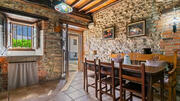 Un interior rústico de piedra con una mesa y sillas de madera, una ventana con vistas, y una puerta que da al exterior.