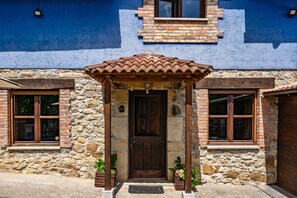 Un edificio de piedra con puerta de madera, dos ventanas y tejado de tejas.