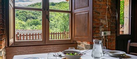 A dining table set with plates, cutlery, and a pitcher, with a view of greenery through a window.