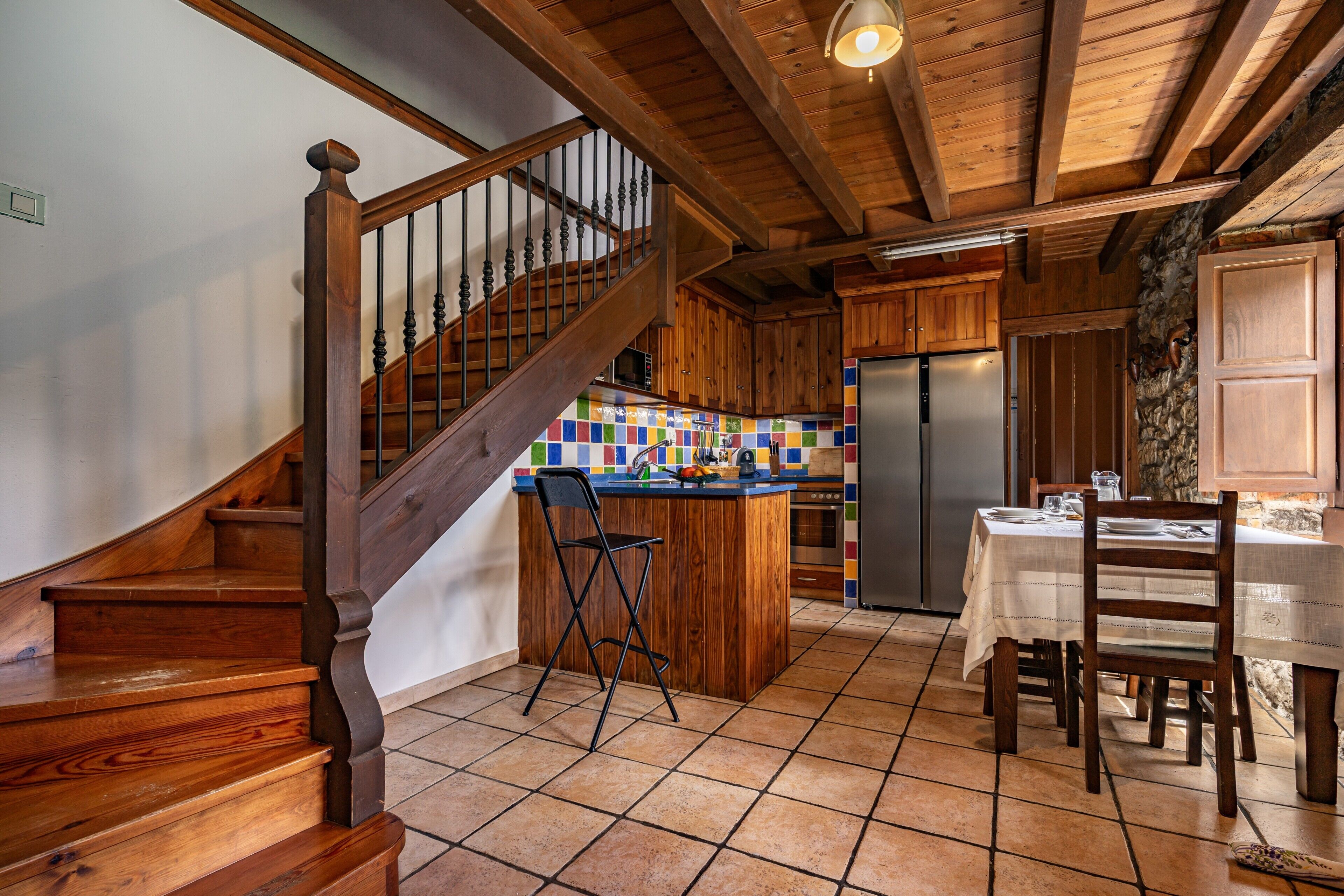 A wooden staircase, kitchen island, dining table, and chairs.