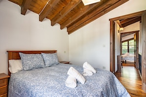 Une chambre avec un plafond en bois, un lit recouvert d’une literie à motifs et deux serviettes posées sur le lit.