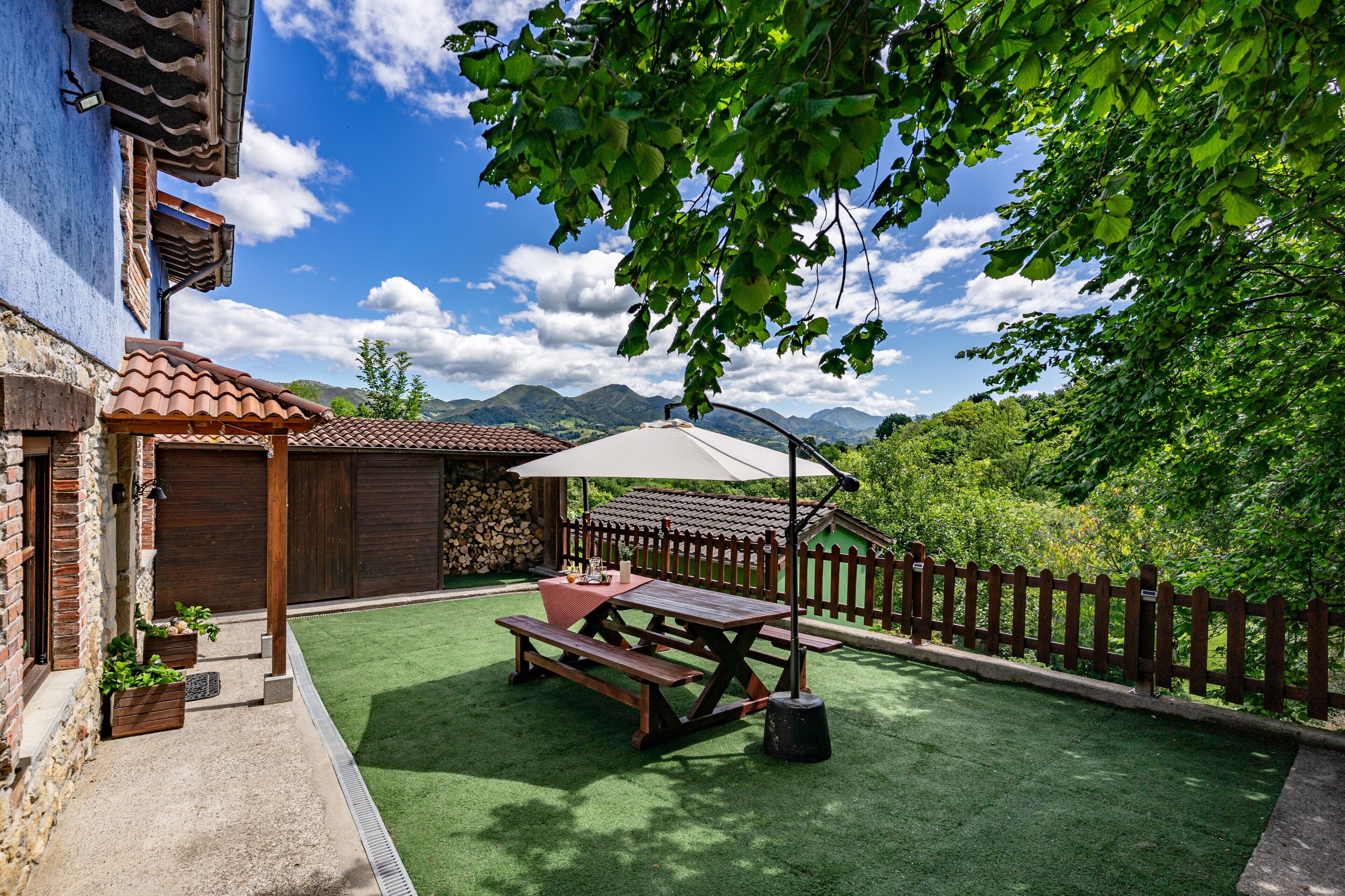 Un patio con una mesa de picnic y sombrilla, rodeado de una valla de madera y vegetación.