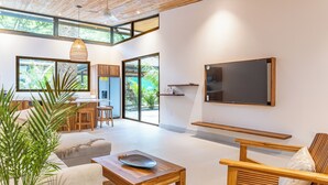 A modern living room with a large window, a wooden coffee table, a sofa, and a TV mounted on the wall.