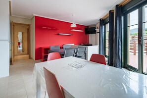 Un espace repas comprenant une table, des chaises, un mur rouge et un téléviseur fixé au mur.